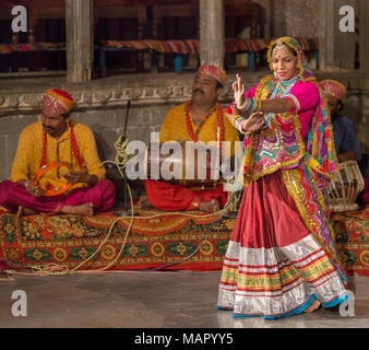 Eine indische Frau trägt einen bunten Kostüm führt eine Rajasthani Folk Tanz, mit Musikern, die akustische Instrumente spielen, Udaipur, Rajasthan, In Stockfoto