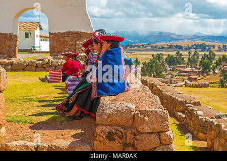 Eine Gruppe von indigenen Quechua Frauen sitzen auf einer alten Inka Wand während einer gesellschaftlichen Zusammenkunft in Chincheros in der Nähe der Stadt Cusco, Peru, Südamerika. Stockfoto