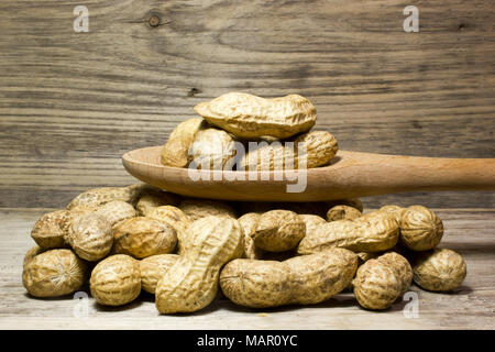 Erdnüsse in der Schale und Löffel aus Holz auf Holz- Hintergrund Stockfoto