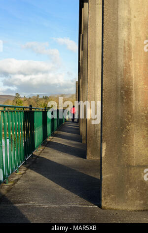 Einsame Person in roter Jacke, die auf der Hängebrücke, The Sound, Kenmare, Irland läuft. Stockfoto