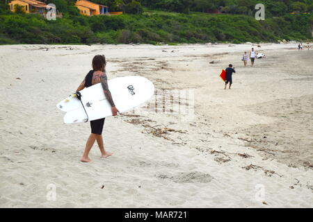 Surfer tätowiert trägt eine weiße Surf Board zu Fuß am Sandstrand in Mexiko Stockfoto