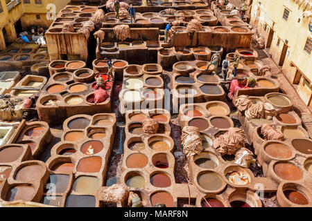 Marokko Fes Medina Souk CHOUWARA GERBEREI GERBEREIEN DER ARBEITER UND kreisförmigen Fässer oder Tanks mit verschiedenen bunten Farbstoffe enthalten, die Häute ansehen Stockfoto