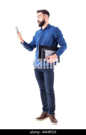 Junge Erwachsene business Mann mit Notebook und Tablet-PC unter dem Arm Kontrolle Handyempfang. Voller Körper auf weißem Hintergrund. Stockfoto