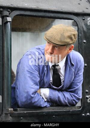 Das Porträt einer Dampfmaschine Treiber im blauen Overall aus dem Kabinenfenster eines schwarzen Dampfzug lehnend. Stockfoto