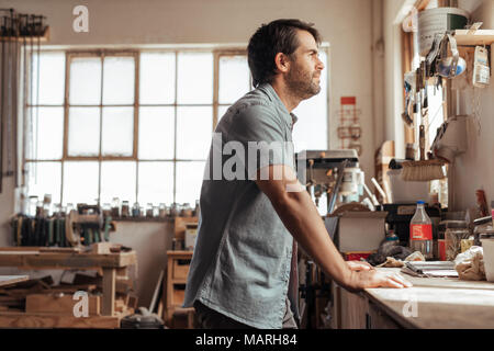 Qualifizierte junge Schreiner auf einer Werkbank lehnte sich tief in Gedanken Stockfoto