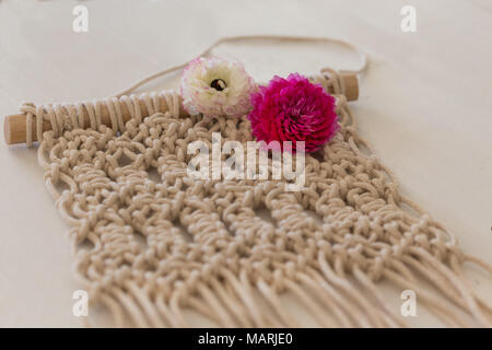 Macrame Wand Kunst der beige Farbe Festlegung auf weißen Tischplatte mit etwas Frühling Blumen Stockfoto