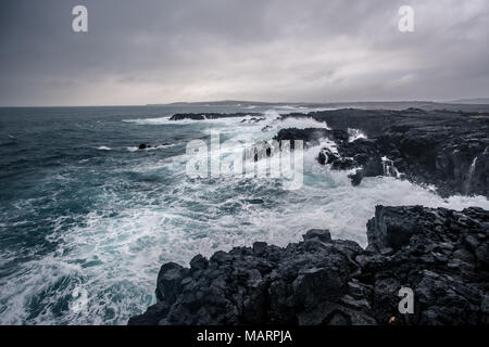 Robuste isländischen Küste mit großen Wellen schlagen die schwarzen Felsen an bewölkten Abend in South West Island. Stockfoto