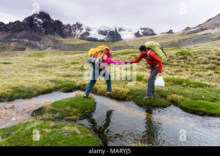 Männliche Bergsteiger hilft weiblichen Partner ein kleiner Bach in der Cordillera Blanca in Peru Kreuz Stockfoto