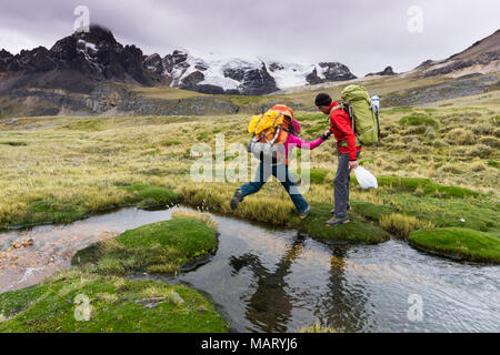 Männliche Bergsteiger hilft weiblichen Partner ein kleiner Bach in der Cordillera Blanca in Peru Kreuz Stockfoto