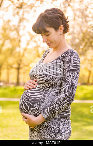 Schwangere Frau in einem Park ihre Holding Bauch, Großbritannien Stockfoto