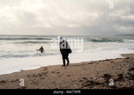 Gyllyngvase Beach, Falmouth. 4 Apr, 2018. UK Wetter: Surfer braves kaltes Wasser bei Gyllyngvase Beach, Falmouth. Eine Frau die Spaziergänge entlang der Falmouth von Gyllyngvase Beach als Surfer das Wasser Credit eingibt: Mick Buston/Alamy leben Nachrichten Stockfoto