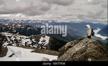 Weibliche Wanderer Wandern auf einem Bergrücken mit Schnee Banken im frühen Frühling. Dramatische und schöne Landschaft im Hintergrund (Gold Bridge, BC, Kanada Stockfoto