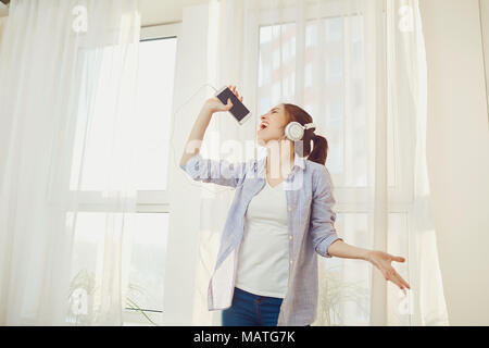 Ein Mädchen in Kopfhörer singt ein Lied gegen das Fenster. Stockfoto