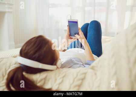 Ein Mädchen in Kopfhörer schaut in das Telefon. Stockfoto