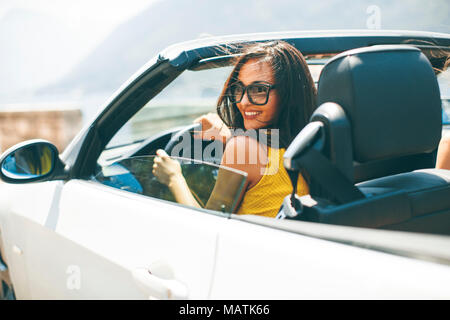 Hübsche junge Frau mit Sonnenbrille im weißen Cabrio Auto fahren Stockfoto