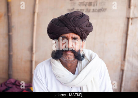 Porträt eines älteren Rajasthani-Mannes, der in einem Zelt auf der Pushkar-Kamelmesse sitzt, mit braunem Turban und Schnurrbart, Indien. Stockfoto