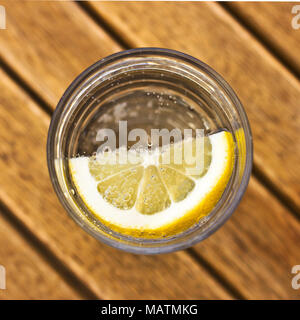 Kohlensäurehaltige Mineralwasser mit Zitrone im Glas mit Blasen auf einem braunen Holztisch Stockfoto