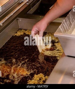 Ein Fischfilet, das in eine Fritteuse in einem Fish and Chip Shop, Hastings, East Sussex, gelegt wird. Stockfoto