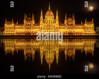 Ungarisches Parlament Gebäude (Budapest) bei Nacht im Wasser der Donau und bei Vollmond darüber reflektiert Stockfoto