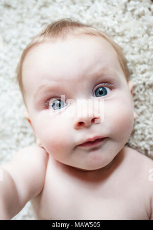 Ein sechs Monate altes Baby Festlegung auf einem weissen Teppich. Stockfoto