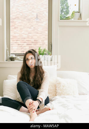 Ein Porträt einer Frau mit langem Haar sitzt auf einem Bett. Stockfoto