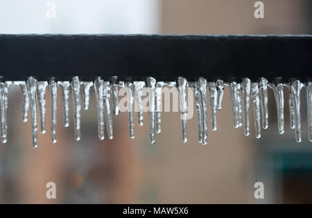 Nahaufnahme von Eiszapfen hängen an Eisen Reihe der Balkon im Haus, Eis überzogen Hintergrund. Stockfoto