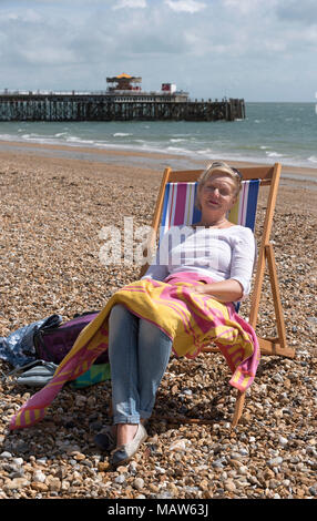 Frau sitzt in einem Liegestuhl am Strand an einem windigen Tag. Fareham, England Großbritannien Stockfoto