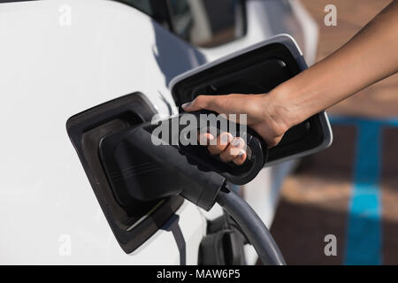 Frau laden Elektroauto an der Ladestation Stockfoto