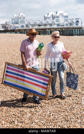 Ältere Paare gehen mit einem Liegestuhl auf einen Kiesstrand. Fareham, England Großbritannien Stockfoto