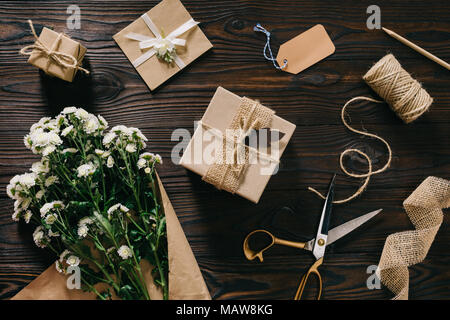 Flach mit eingepackten Geschenke, Blumenstrauß, Seil und Schere auf Holz- Oberfläche Stockfoto