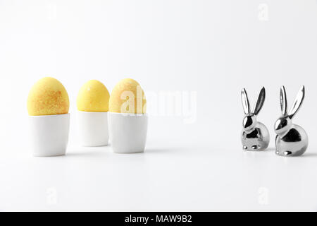 Gelb bemalte Ostereier in Ei steht und Statuetten von Kaninchen auf Weiß Stockfoto