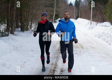 Paar, Jogger, Mann und Frau sind Joggen in einem Wald Straße im Winter. Stockfoto
