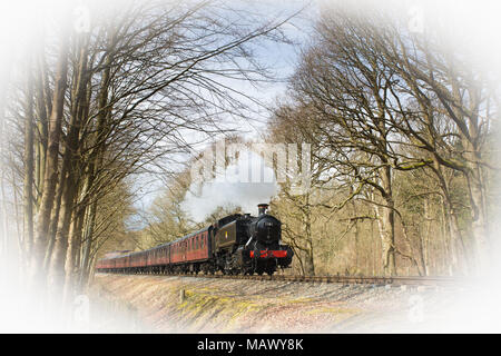 Altmodische, alte britische Dampfeisenbahn, die bei Frühlingssonne durch die Waldlandschaft zieht. Stockfoto