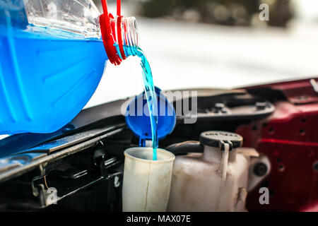 Nach der Abfüllung Frostschutzmittel Flüssigkeit der Scheibenwaschanlage in schmutzigen Auto von Blau und Rot Frostschutzmittel Behälter Detail. Stockfoto