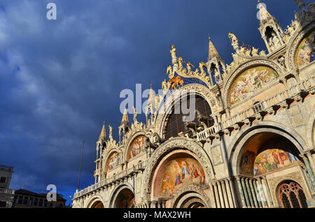 Schöne gotische und byzantinischen Fassade der Basilika von St. Markus in Venedig glänzt bei Sonnenuntergang mit bewölktem Himmel Stockfoto