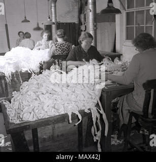 1950er Jahre, historische Frauen, die in einer kleinen Baumwollmühle arbeiten, die sich an Bänken gegenübersitzen und große Bündel von Überresten oder Materialabschnitten aussortieren, möglicherweise Baumwolle, England, Großbritannien. Stockfoto