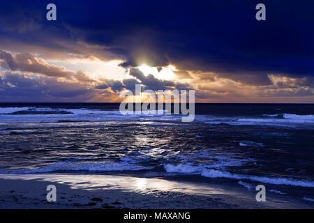 Sea Scape mit Wellen und dramatischen dunkle Wolken mit einer Welle von Sonnenstrahlen bei Sonnenuntergang Stockfoto