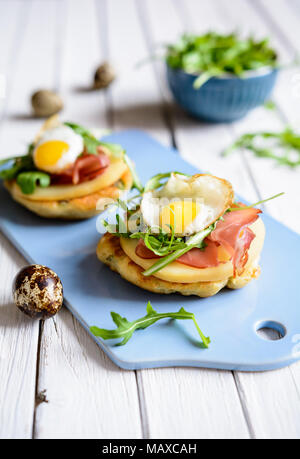 Herzhafte Joghurt und Schalotten Pfannkuchen mit Schwarzwälder Schinken, geräucherter Käse, Scheiben, Wachtelei und Rucola Stockfoto