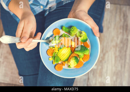 Das Mädchen hält einen Teller mit Gemüse. Gesunde Ernährung Konzept. Ein Mädchen in Jeans und ein kariertes Hemd. Lässigen Stil. Die richtige Ernährung. Diät. Gesundheit. Veget Stockfoto