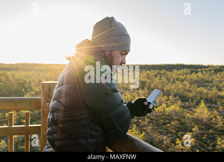 Bärtiger Mann am Smartphone gegen Herbst Wald in Sun Beam Lebensstil im Freien und Smartphone Konzept suchen Stockfoto