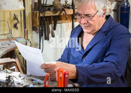 Ein männlicher Arbeitnehmer sucht eine Rechnung an seinem jewerly Workshop, Sorge, besorgt. Stockfoto