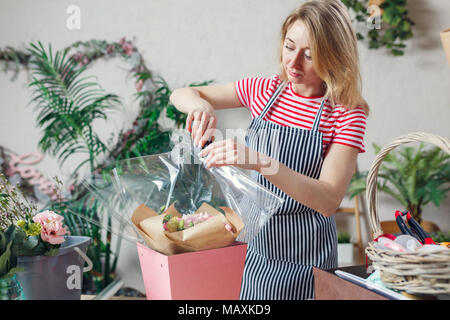 Bild junger Floristen mit Hefter dekorieren florale Komposition am Tisch mit Blumen, Boxen Stockfoto