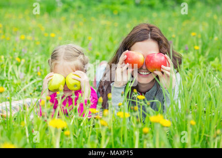 Mutter und Tochter auf grüner Wiese liegend und mit Äpfeln Stockfoto