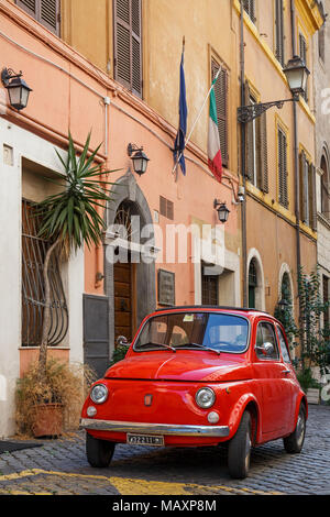 Eine ikonische alten roten Fiat 500 in einer gepflasterten Straße in Rom, Italien, außerhalb eines Gebäudes unter italienischer Flagge geparkt. Stockfoto