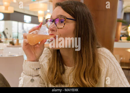 Junge Frau mit Gläsern, die Fruchtsaft trinkt und im Winter einen weißen Strickpullover trägt Stockfoto