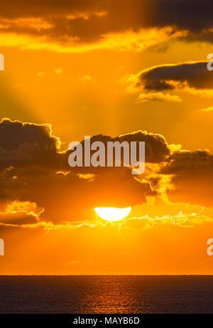 Sonnenuntergang über dem Meer mit Strahlen von der Sonne durch die Wolken wie die Wolke deckt teilweise die niedrige Sonne. Stockfoto