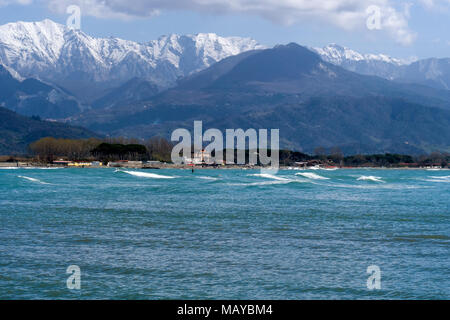 Wellen und nicht identifizierbare Surfer. Mittelmeerküste in der Nähe von Massa Carrara. Die apuanischen Alpen im Hintergrund. Stockfoto