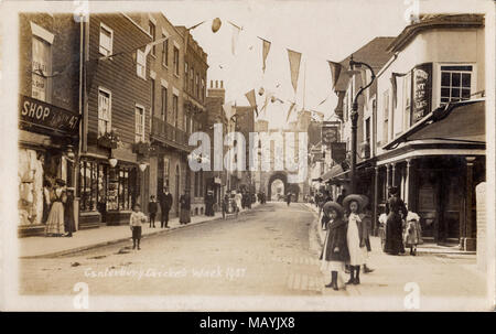 Sepia Postkarte von Canterbury, Cricket Woche 1907 zeigt die Westgate Towers und wimpelketten in St. Peter Street. Bild gescannt aus einer alten Postkarte. Edwardian Straße Szene mit Moden Damen, Schaufenster, Milch Warenkorb. Kricket Woche ist im August gefeiert und die Straßen sind eingerichtet, um das Ereignis zu markieren. Stockfoto