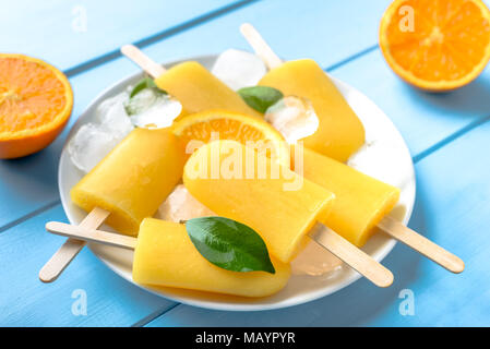 Orange popsicle auf Blau Holz- Hintergrund. Erfrischende Sommer ices auf Stick. Stockfoto