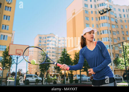 Frau Tennis outdoor, Hot shot Ball. Üben auf dem Tennisplatz am sonnigen Tag, auf eine Stadt Hintergrund Stockfoto